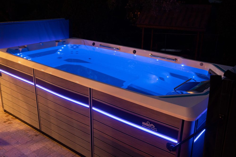 Endless Pools swim spa glowing blue in a backyard at night